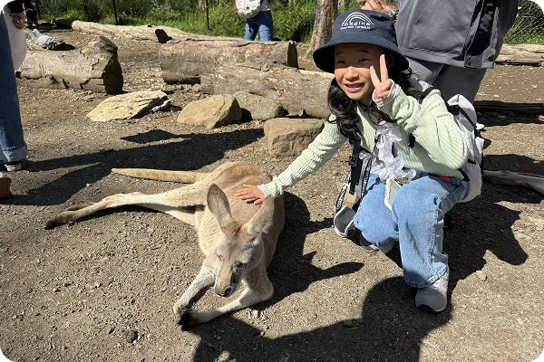 カンガルーに触れて笑顔でピースしている女の子の写真
