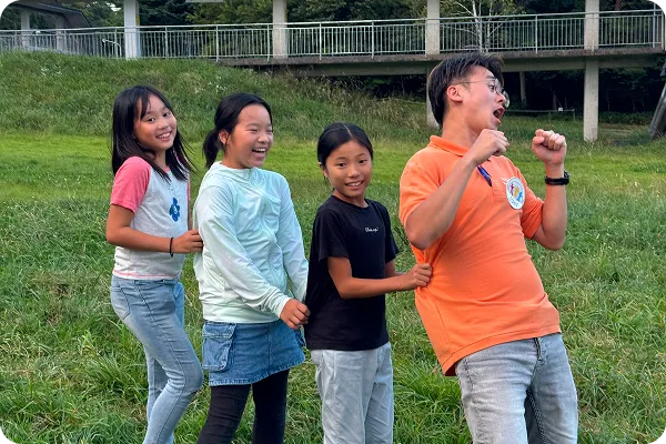 芝生の上で子どもたちが先生の後ろに並んで笑いながら遊んでいる写真