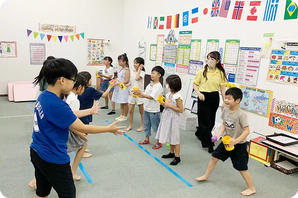 講師と子どもたちが床に引かれたラインを使って体験型の英語学習ゲームを楽しんでいる写真